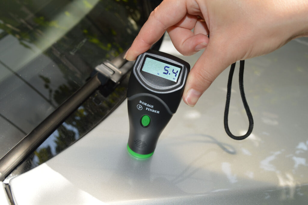 Damage Finder paint thickness tool measuring 5.4 mil on a car panel during used car inspection